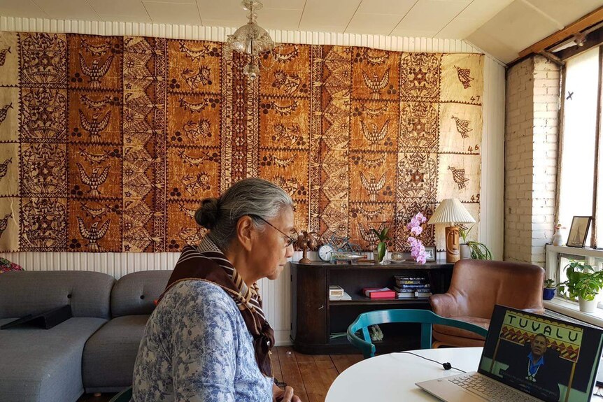 An elderly woman watches Pacific Unite on a laptop in front of a Pacific islands artwork.