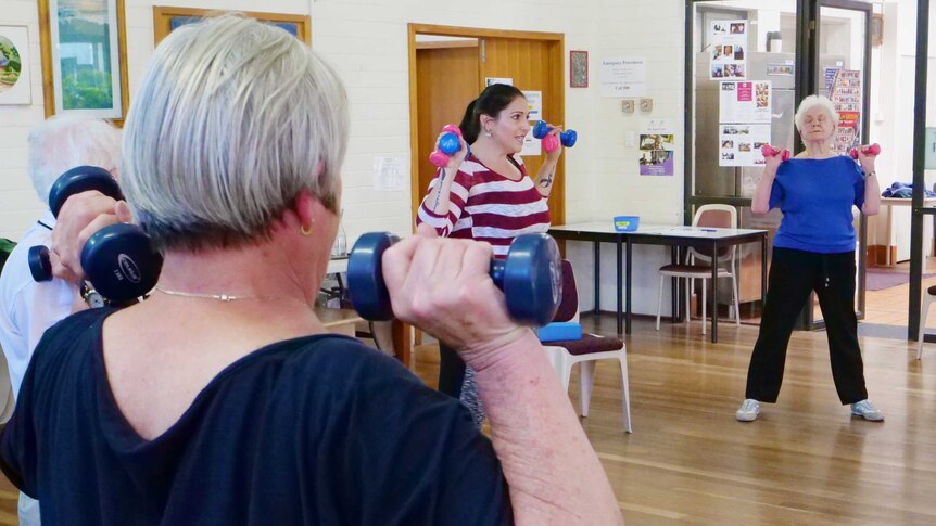 A younger female instructor leads a seniors' exercise program.