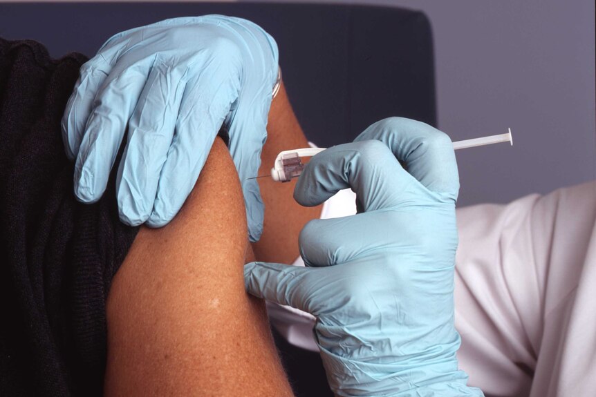 Close up of gloved hands injecting a vaccination into someone's upper arm.