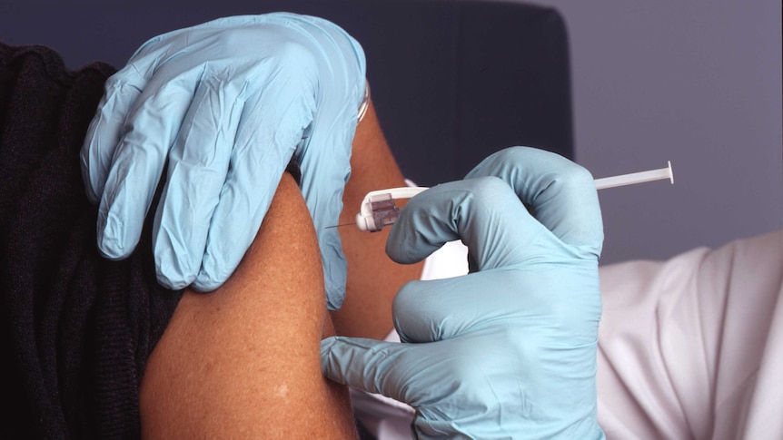 Close up of gloved hands injecting a vaccination into someone's upper arm.