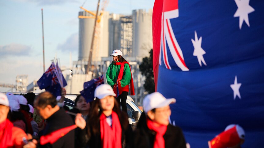 Chinese supporters carrying Australian flags stand in a group in Kwinana with an industrial plant behind them.