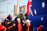 Chinese supporters carrying Australian flags stand in a group in Kwinana with an industrial plant behind them.