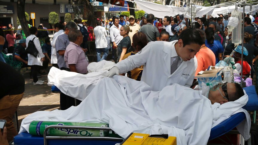 A doctor bends over a man lying in a hospital bed in the middle of a bustling street.