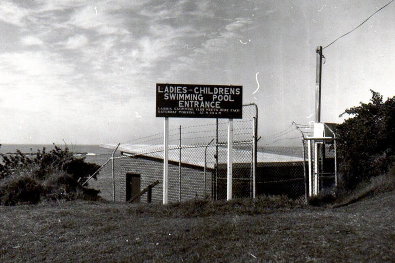A black and white image showing a sign that says "ladies and children's swimming pool entrance". 