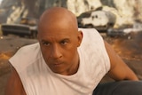 Vin Diesel crouched in front of three cars, with a determined expression, in Fast and Furious 9