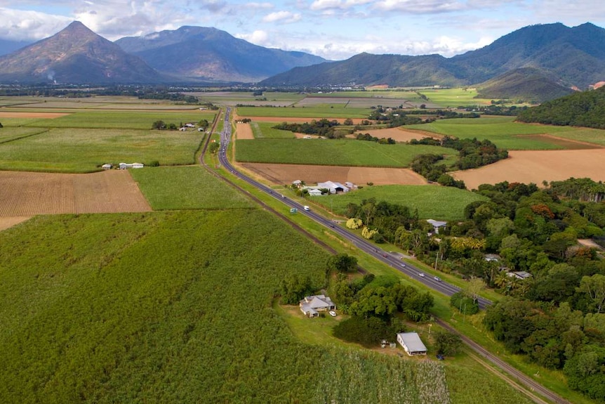 An aerial view of a highway passing through flat country with mountains in the background.