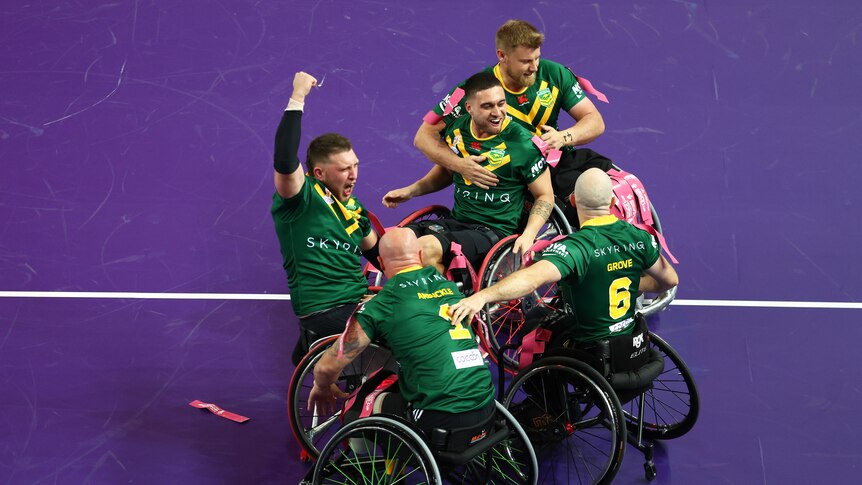 An Australian player closes his eyes and shouts with his fist pumped as teammates celebrate his wheelchair rugby league try.