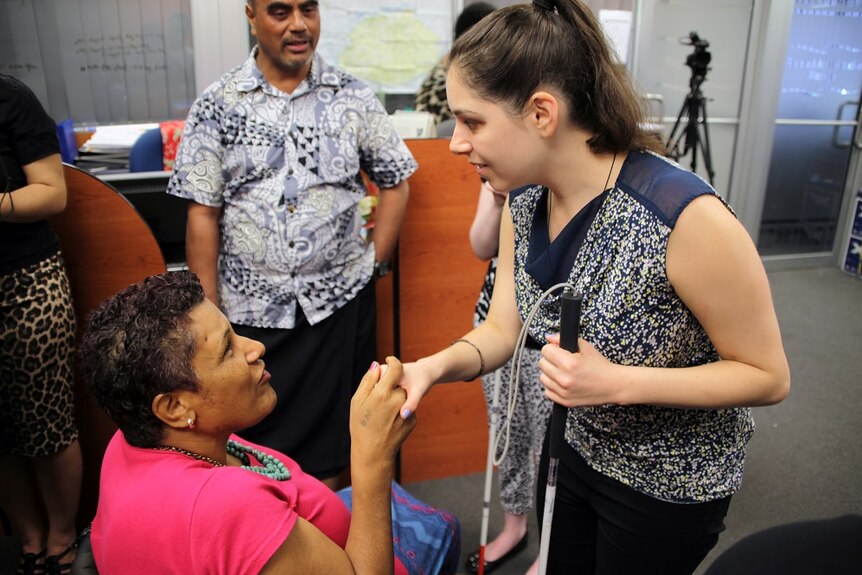 Nastasia Campanella holding cane and shaking hands with a female staff member as a man watches on in an office in Fiji.