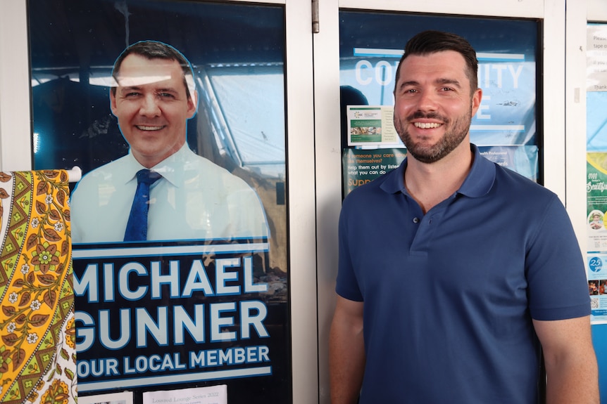 A man smiling and standing next to a door featuring a picture of former NT Chief Minister Michael Gunner. 