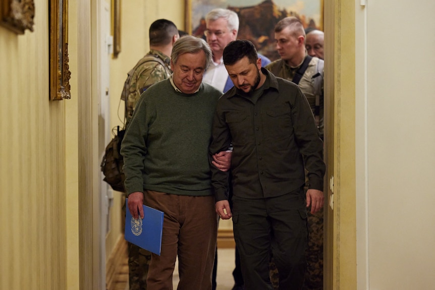 UN Secretary-General Antonio Guterres walks down a corridor holding the arm of ukrainian president volodymyr zelenskyy