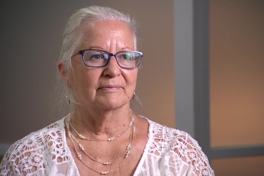 A woman with grey hair and glasses looks off camera.