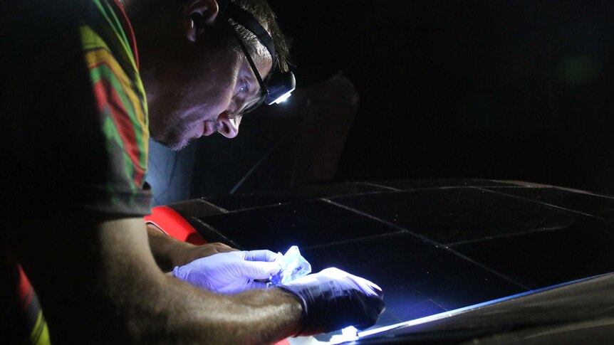 A team member works on the car in the dark, wearing a headlamp.