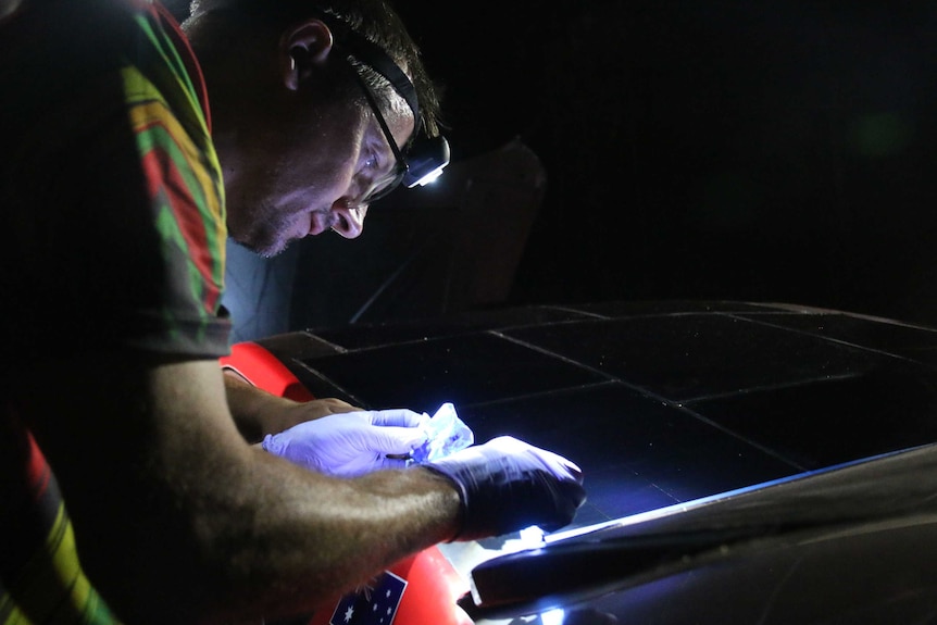 A team member works on the car in the dark, wearing a headlamp.