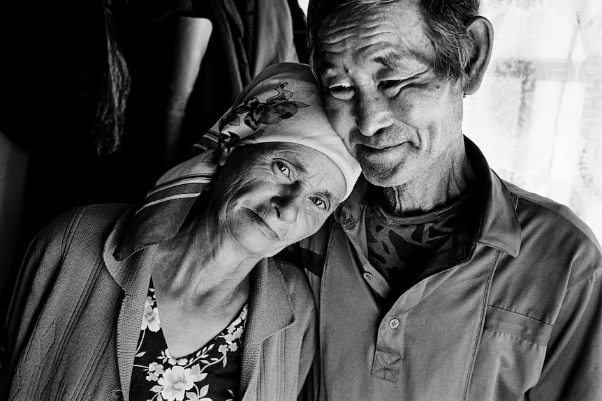 A Ukrainian woman looks into the camera as she rests on her Uzbek husband's shoulder.