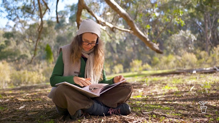 Woman wearing a beanie sitting cross-legged in the bush