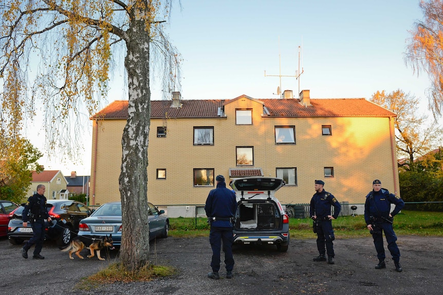 Police officers at the apartment building of the man who attacked Swedish students