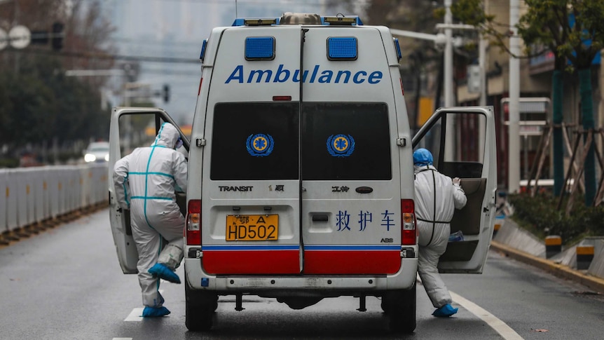 Two paramedic staffs jumping onto an ambulance vehicle on an empty street in Wuhan, China.