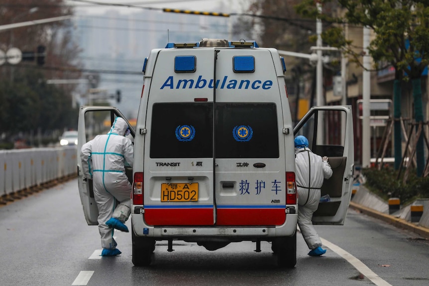 Two paramedic staffs jumping onto an ambulance vehicle on an empty street in Wuhan, China.