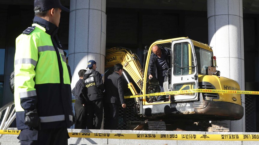Police officers examine an excavator after a man rammed into a gate near a Seoul prosecutors' office in Seoul, South Korea