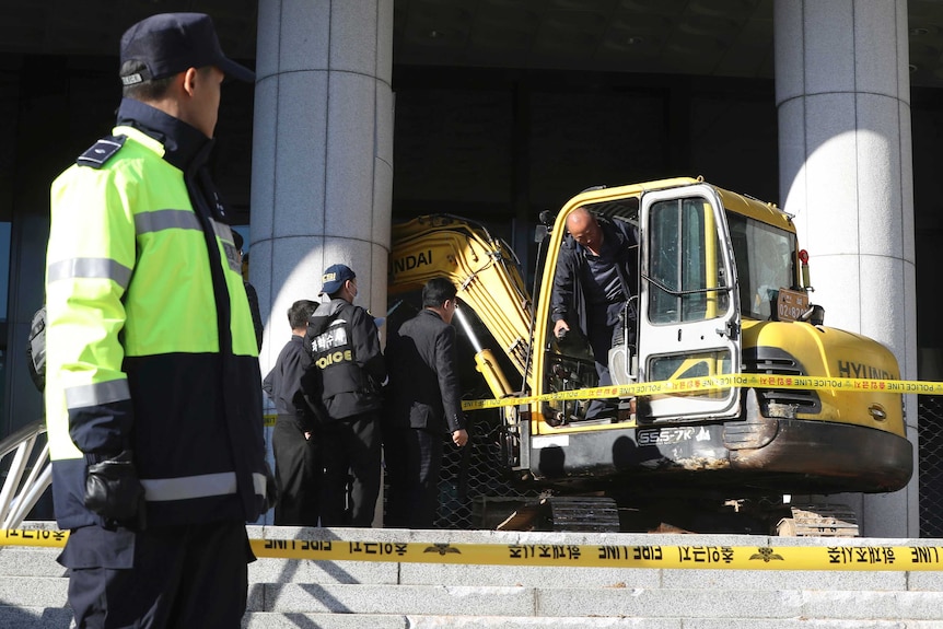 Police officers examine an excavator after a man rammed into a gate near a Seoul prosecutors' office in Seoul, South Korea