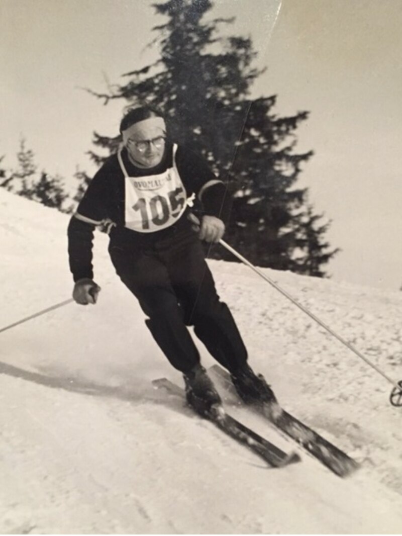 A black and white photo of a man skiing downhill with the number 105 on his chest