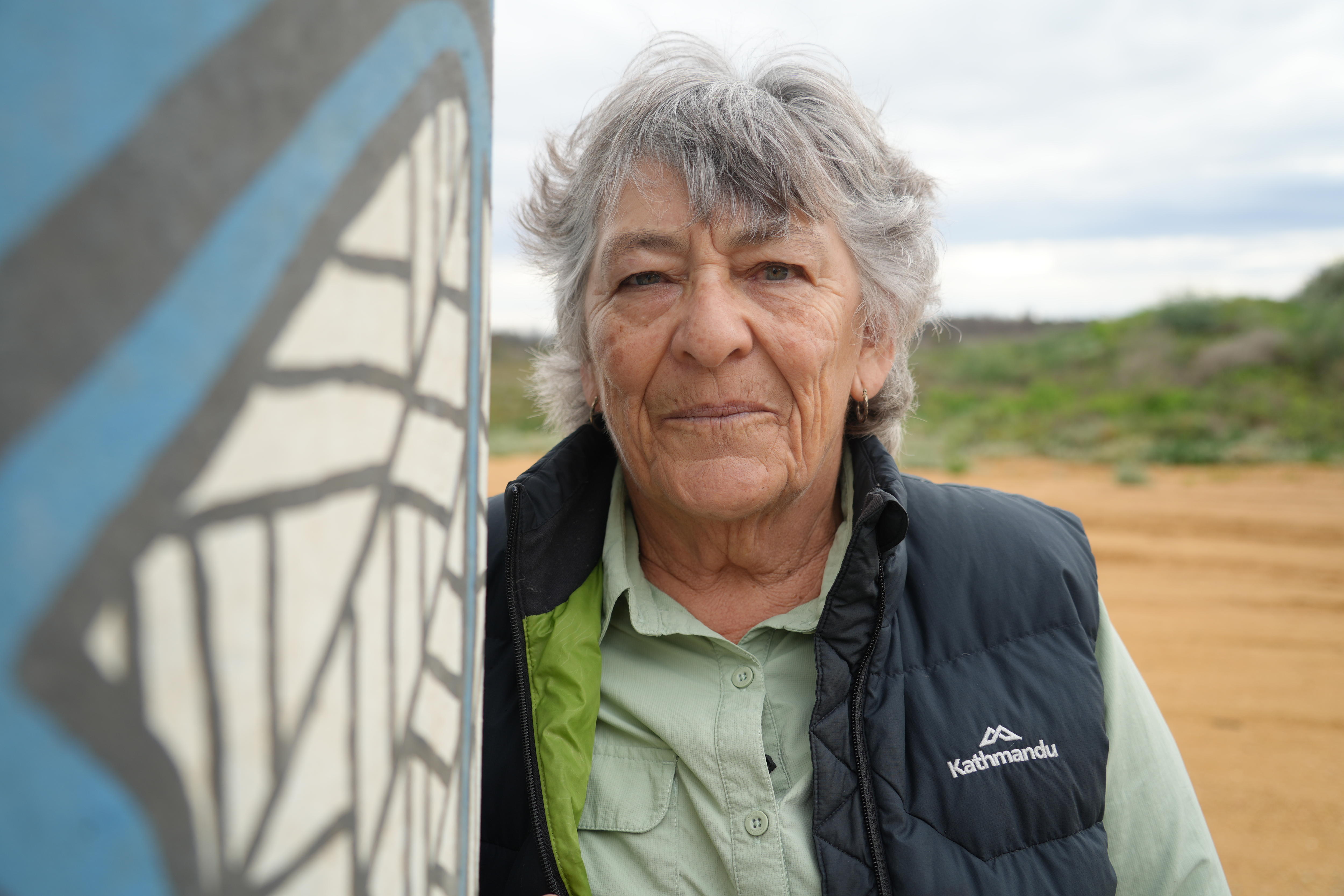 A grey-haired woman stares at the camera 