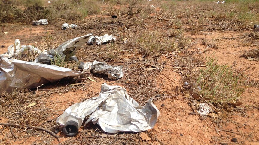 empty cask wine bag lying on a ground of red dust and grass clumps.