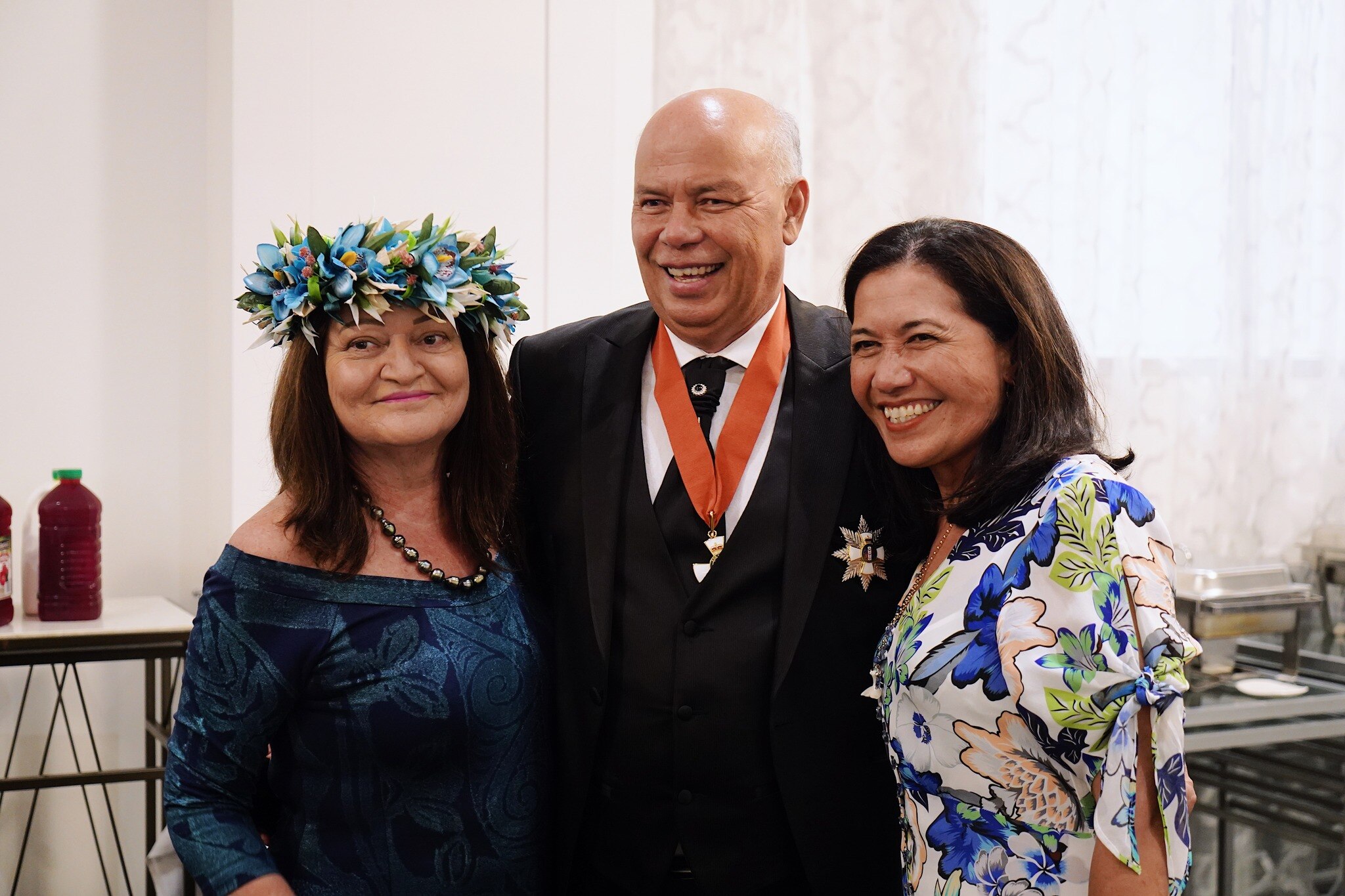 A pacific man with no hair smiling wearing a suit and with a medallion around his neck