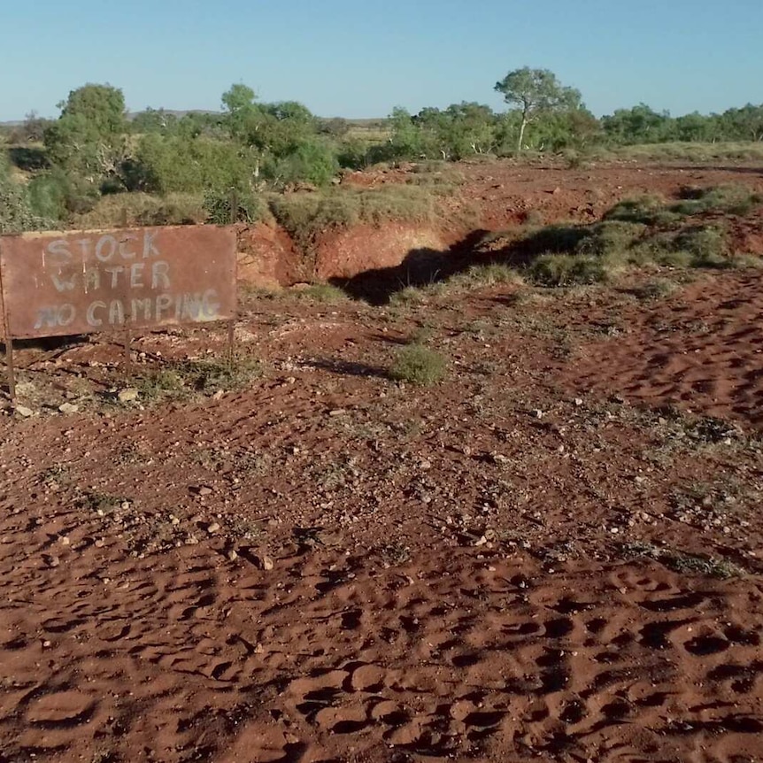 A sign reads "stock water, no camping" near an outback watering hole