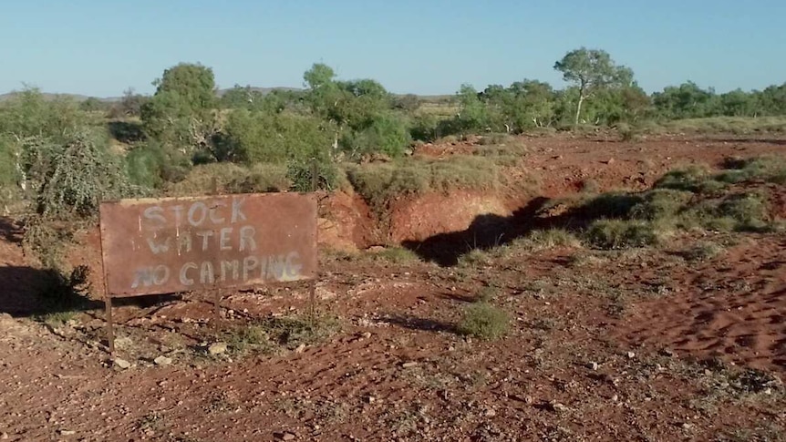 A sign reads "stock water, no camping" near an outback watering hole