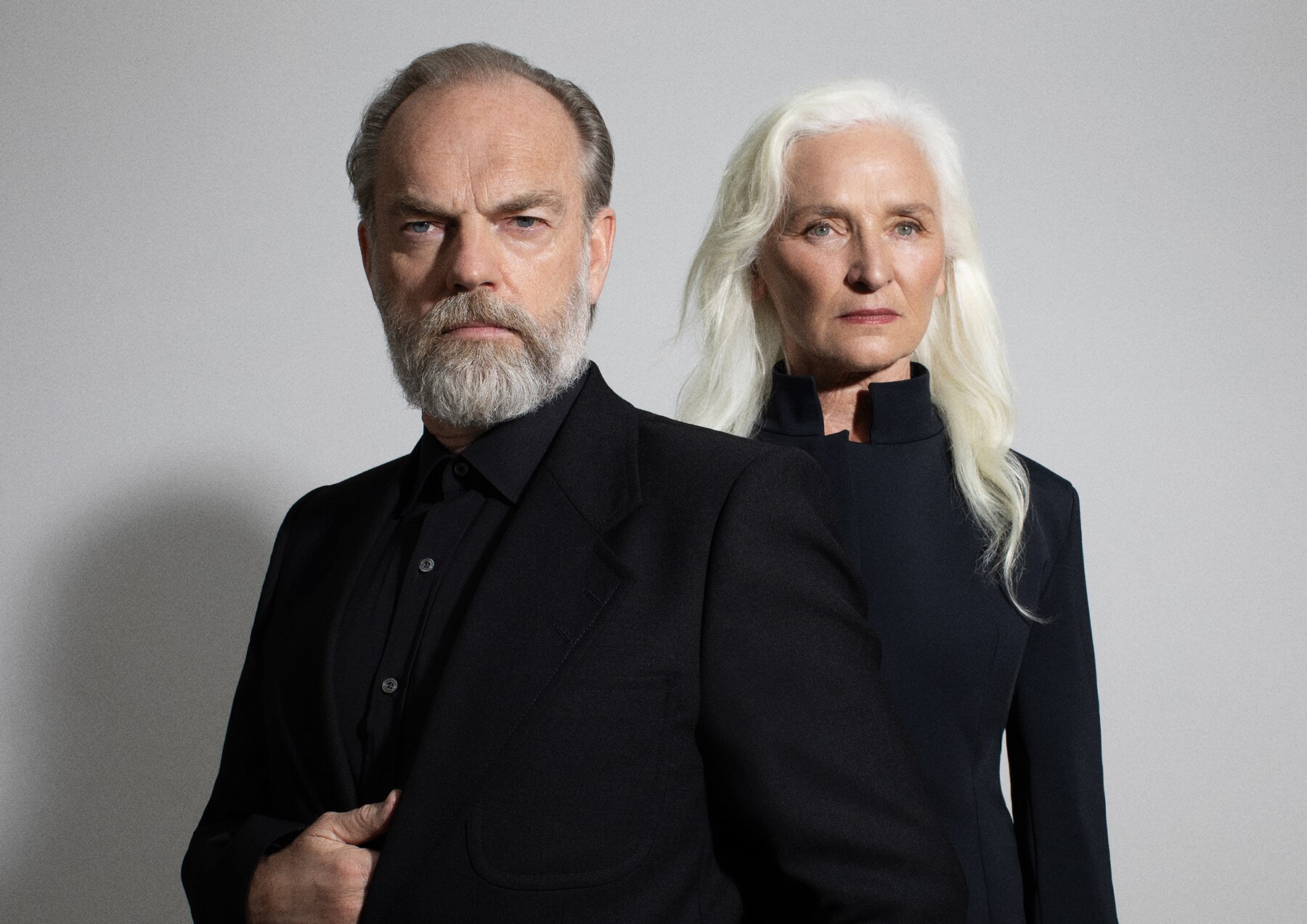Hugo Weaving and Olwen Fouéré pose together. They each have stern expressions, and wear all black.