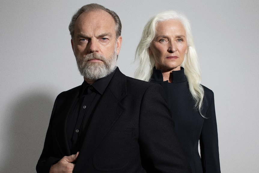 Hugo Weaving and Olwen Fouéré pose together. They each have stern expressions, and wear all black.