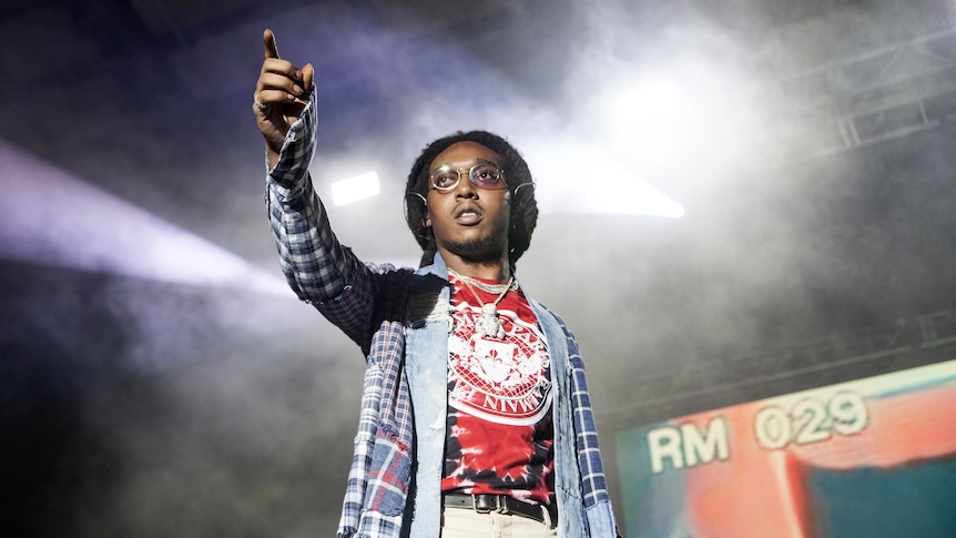 Migos rapper Takeoff performing live and pointing at the crowd with light streaming in behind him