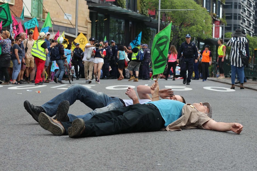 Two man lay on the road and wave a flag as other protesters stand in the background.