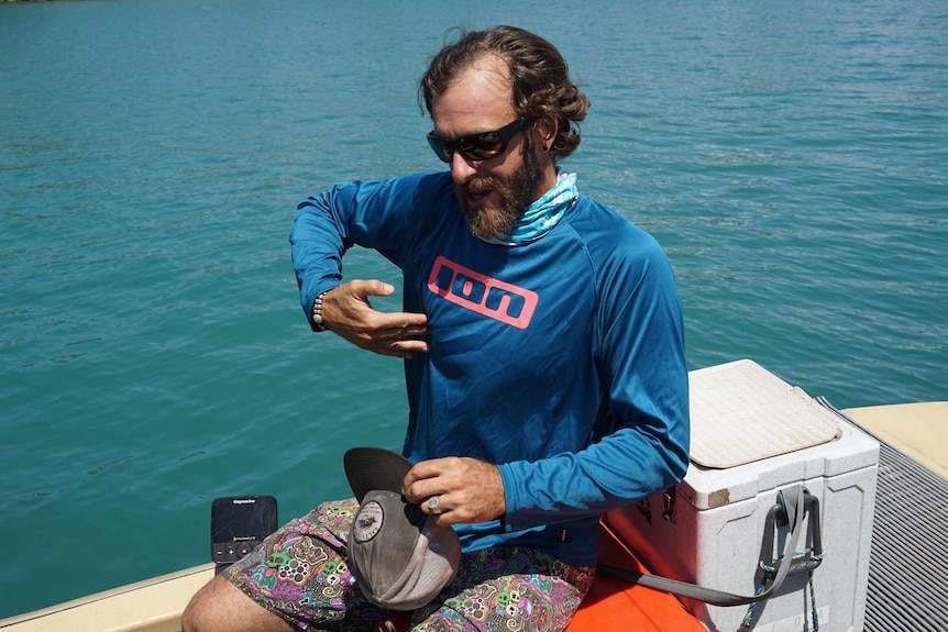 Darwin fisho wearing sunglasses points to his chest on Darwin harbour.