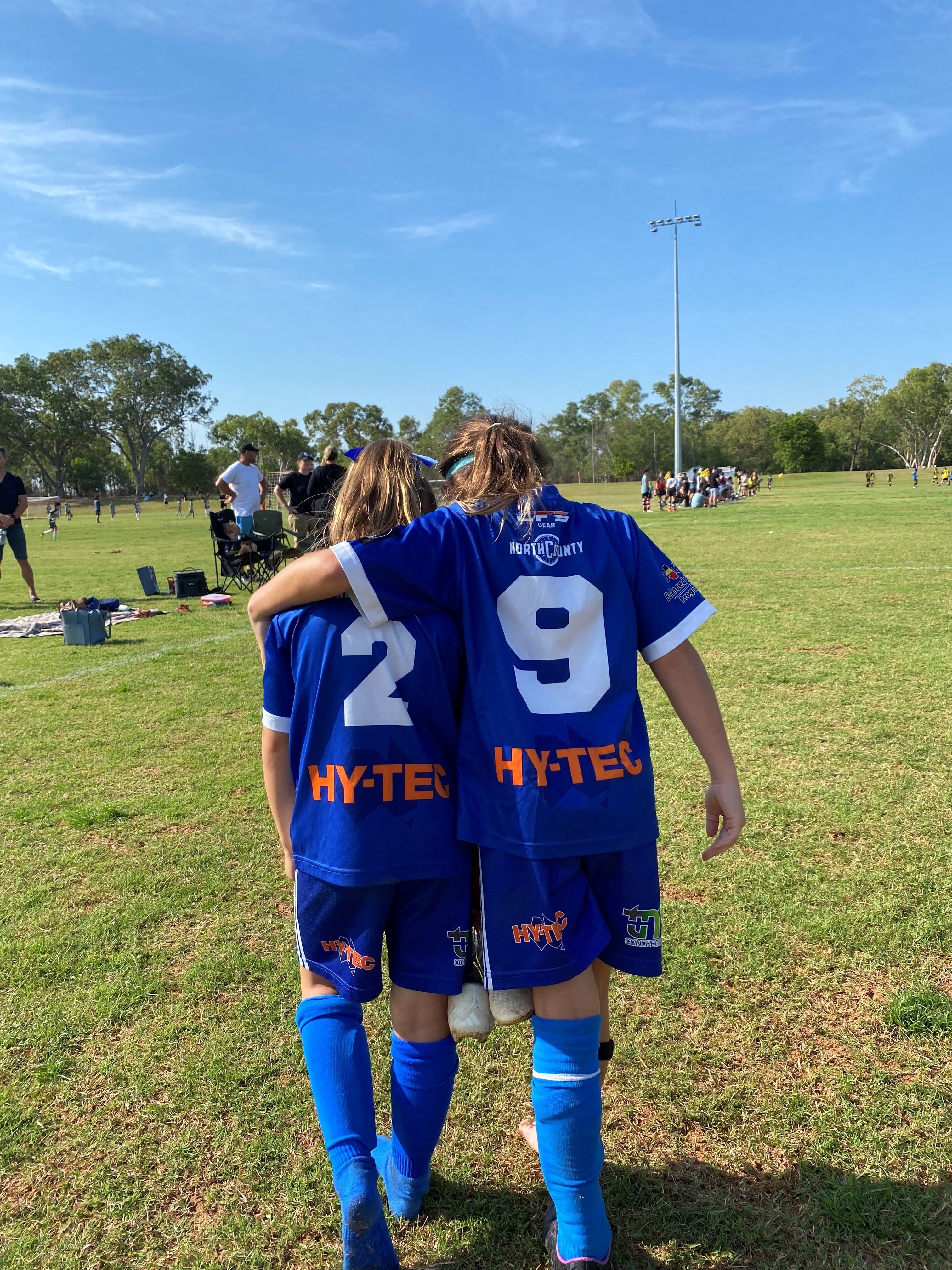 Junior girls soccer teammates walk arm-in-arm off the field in Darwin.