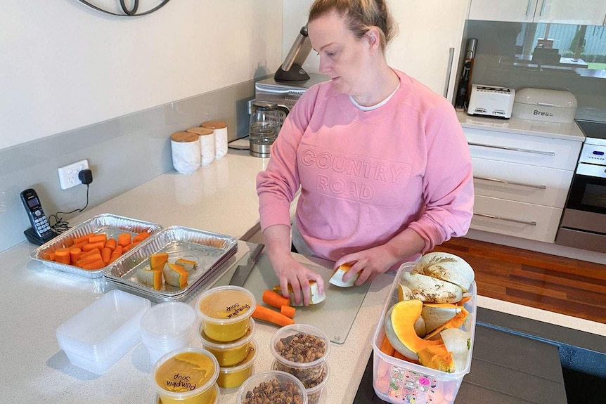 A woman in a kitchen, surrounded by carrots, pumpkins, nuts and vegetable scraps.