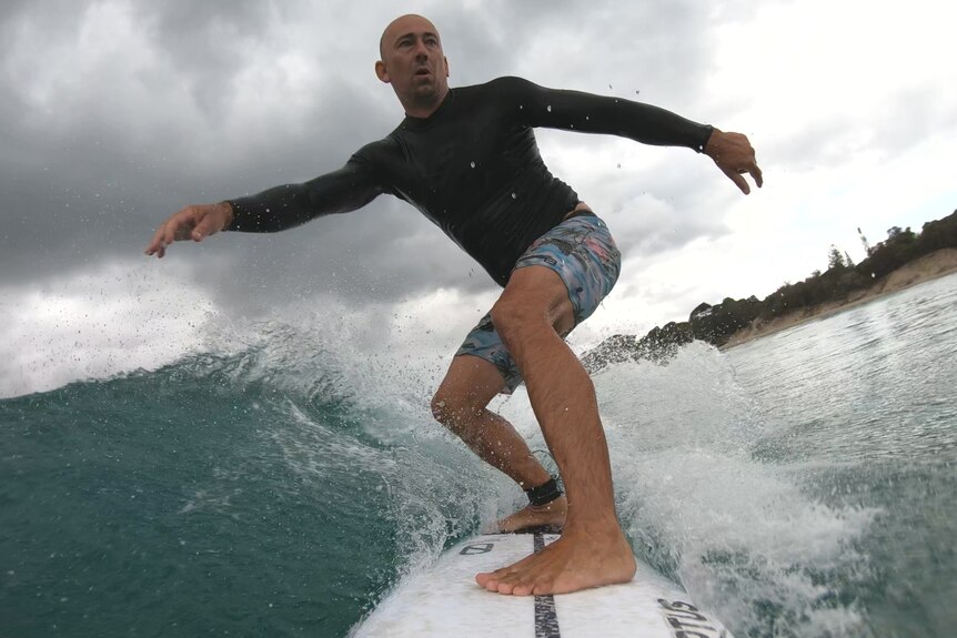 A man in a black rash shirt and board shots on a surboard riding a wave