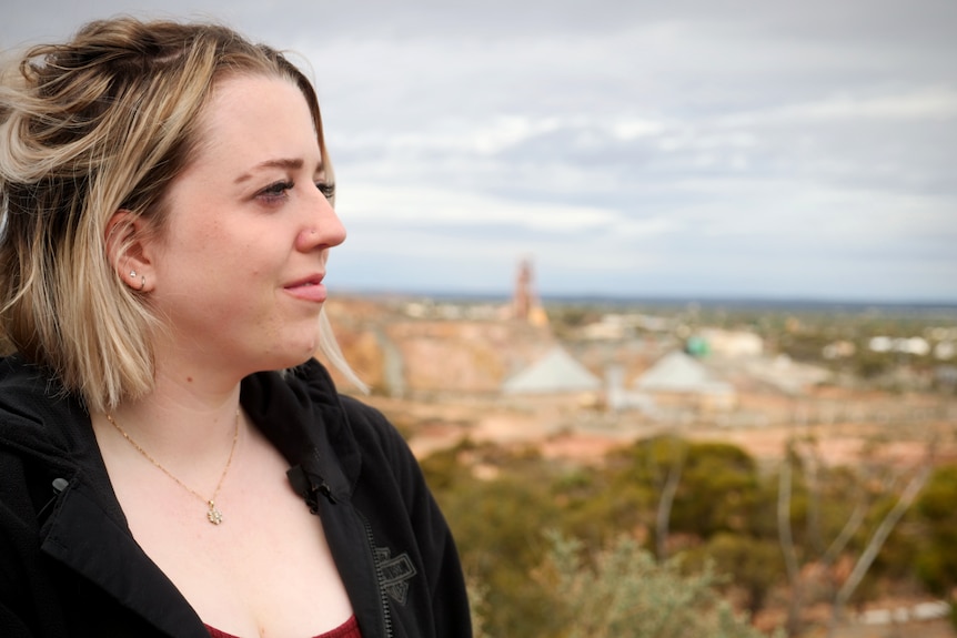 A young woman wearing a dark top in front of an outback town.