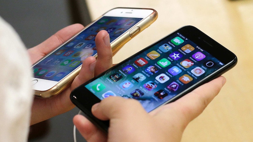 A close-up of two iPhones with colourful screens and countless apps, held by two hands.