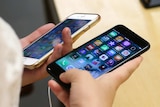 A close-up of two iPhones with colourful screens and countless apps, held by two hands.