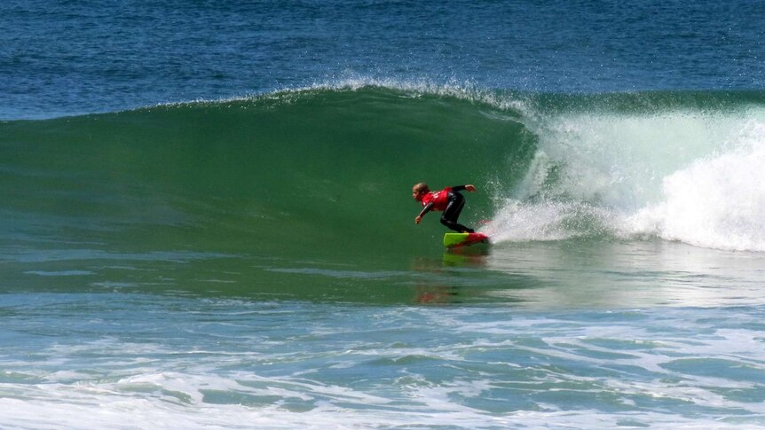 A young girl wearing a wetsuit and red rash vest surfs a wave.