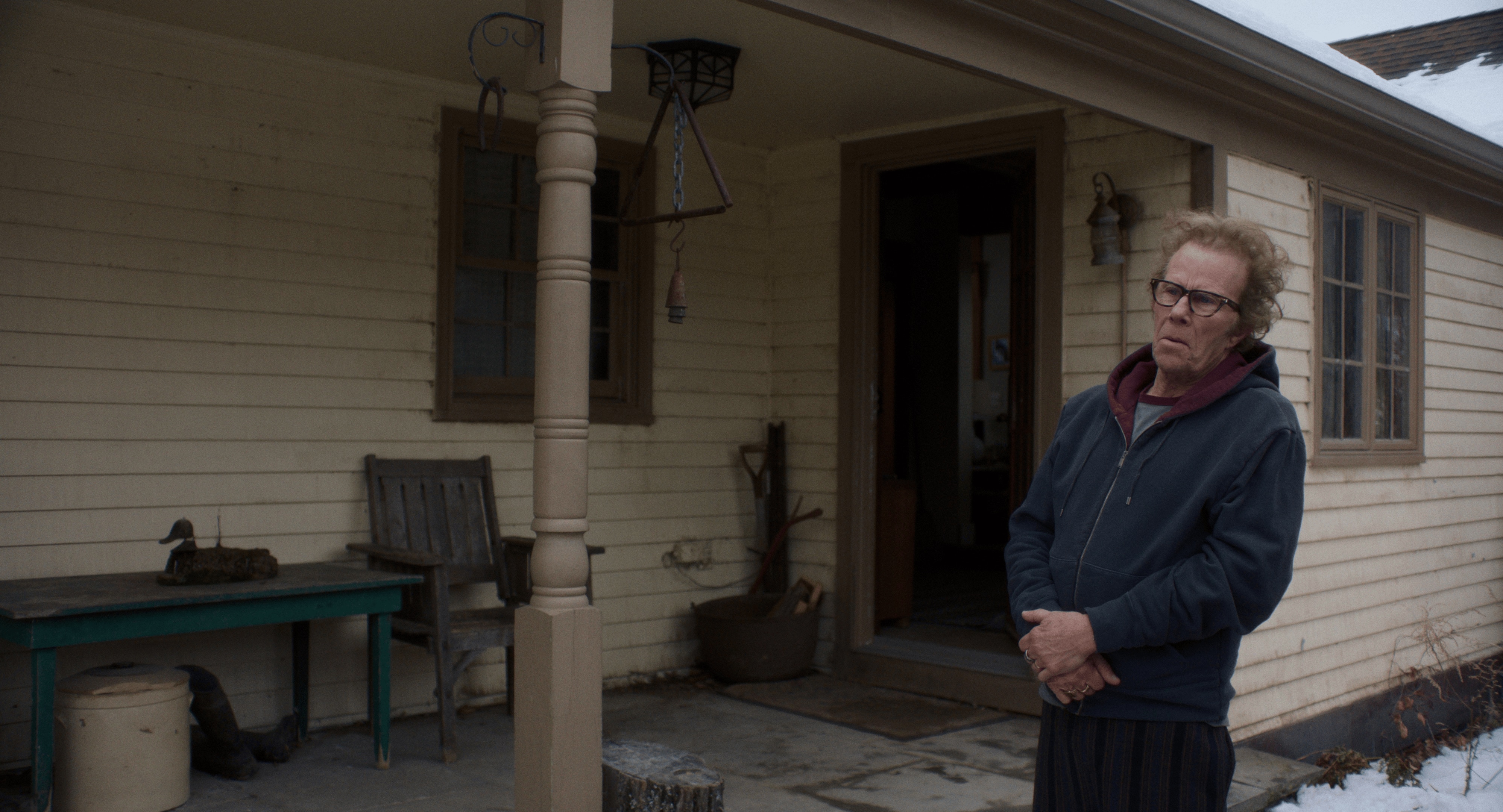 Un hombre se para frente a una casa y mira algo fuera de campo.