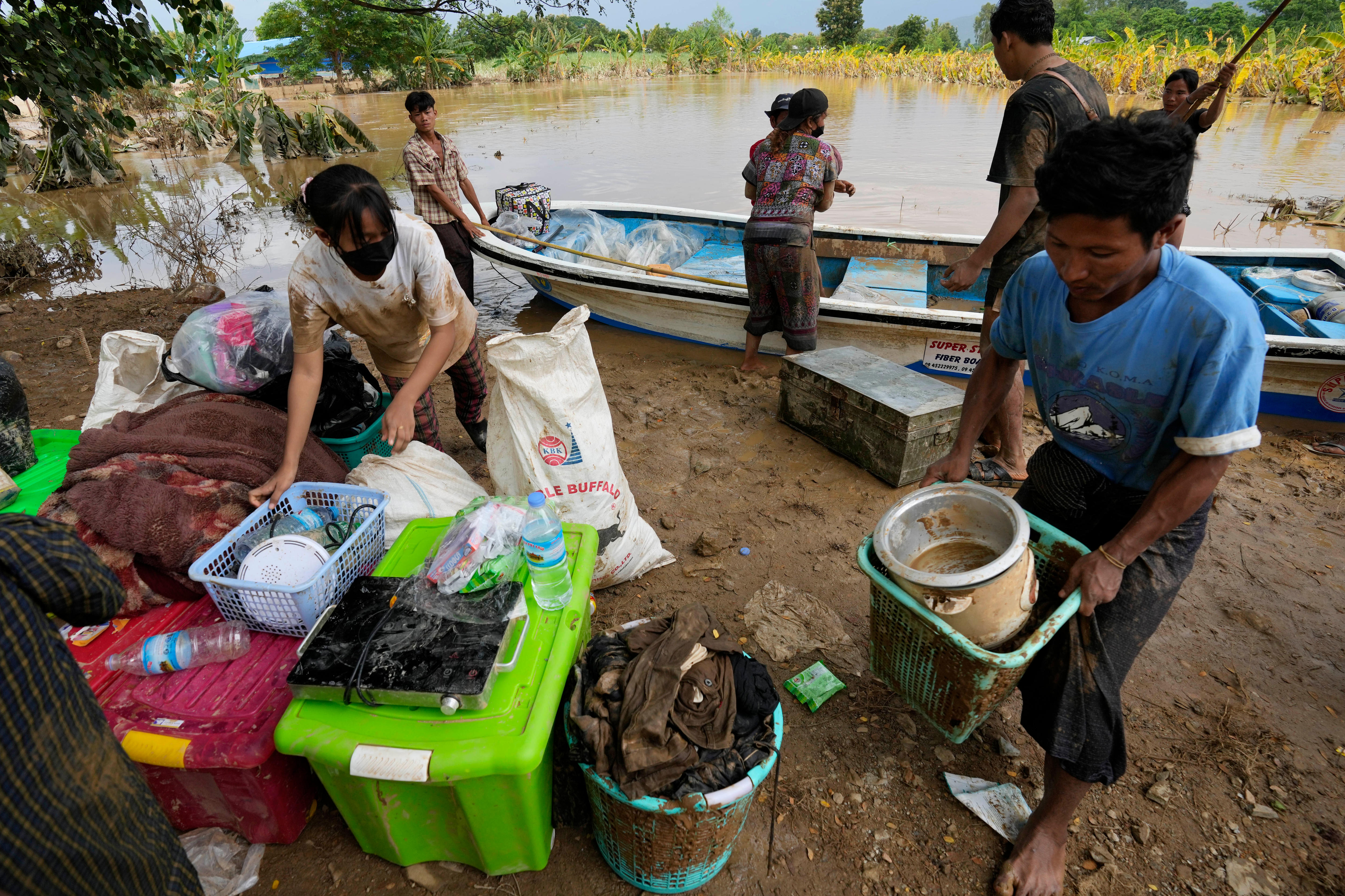 A group of locals pack up their belongings into plastic boxes next to a boat that sits in floodwaters
