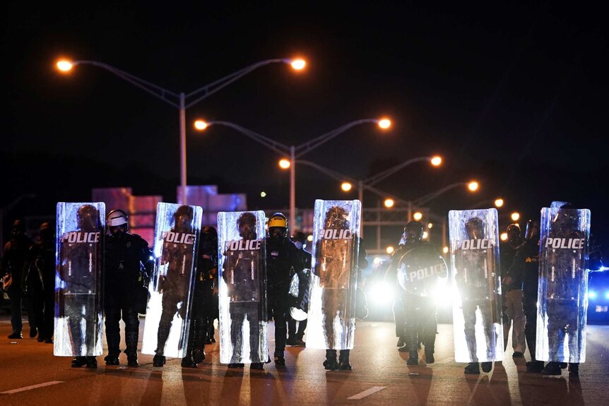 police with shields walk in a line toward on a freeway at night in Atlanta