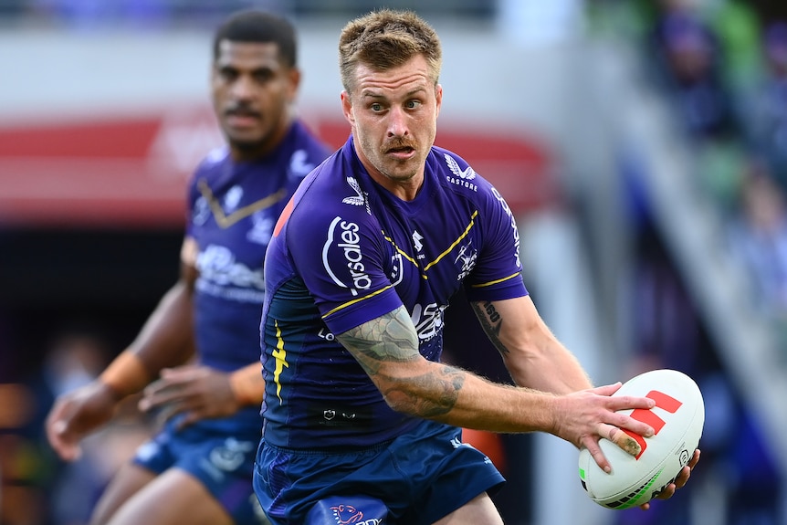 A Melbourne Storm NRL player holds the ball in both hands against Wests Tigers.