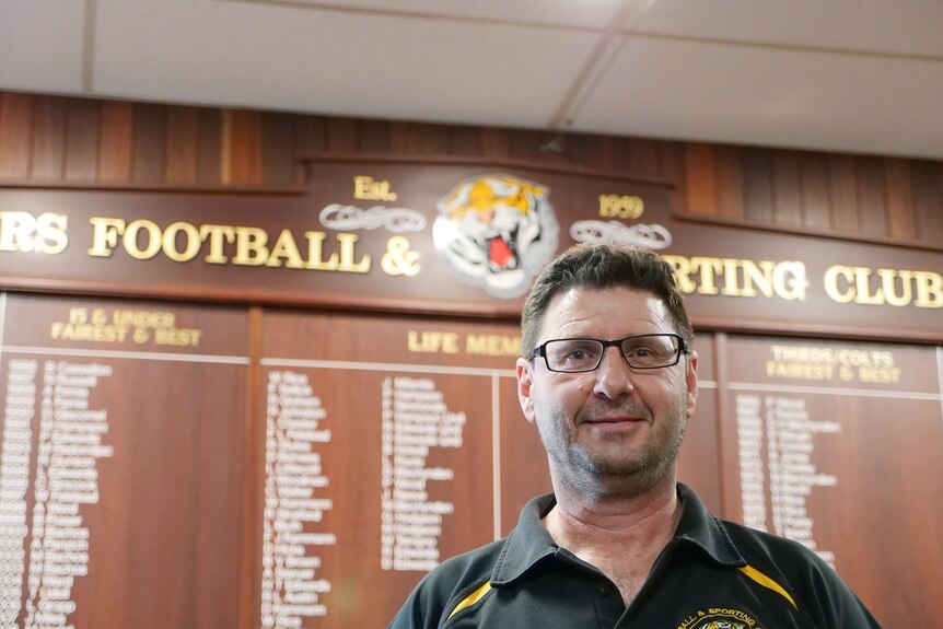 A man stands in front of the honour board at a local Aussie Rules club.
