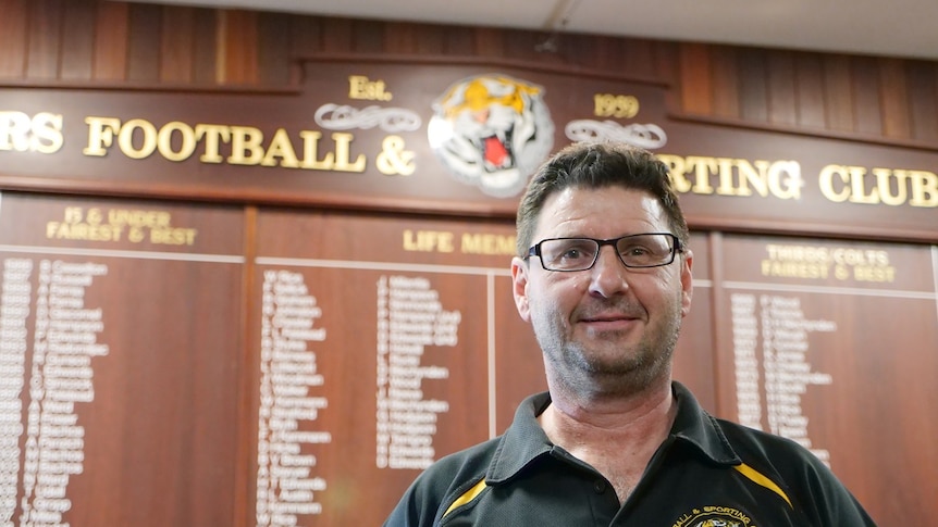 A man stands in front of the honour board at a local Aussie Rules club.