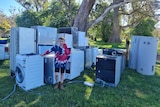 A boy stands in front of a pile of white goods in a back yard.