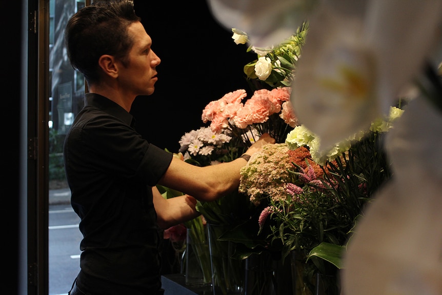 Bart Hassam standing in a florist arranging pink flowers in a vase.